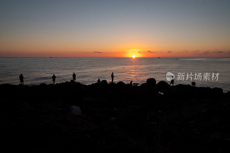 Silhouettes of fishermen on a rocky shore against the background of the sea at sunrise.